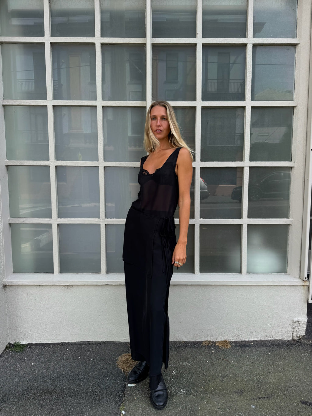 Woman in a black outfit standing in front of a glass-paneled building.