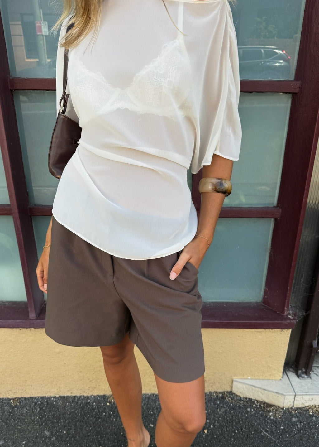 Person wearing a white top and gray shorts standing in front of a building.